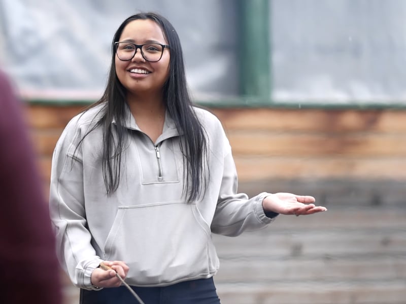 A woman with long dark hair and glasses wearing a light grey sweatshirt