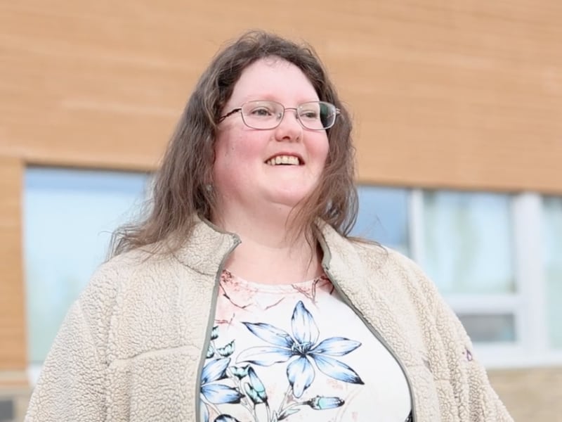 Woman with long hair and glasses wearing a grey fleece jacket and floral shirt