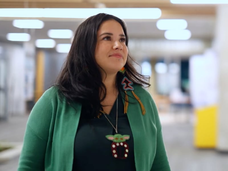 A woman with long dark hair, wearing a black shirt and green cardigan, looking off to the right