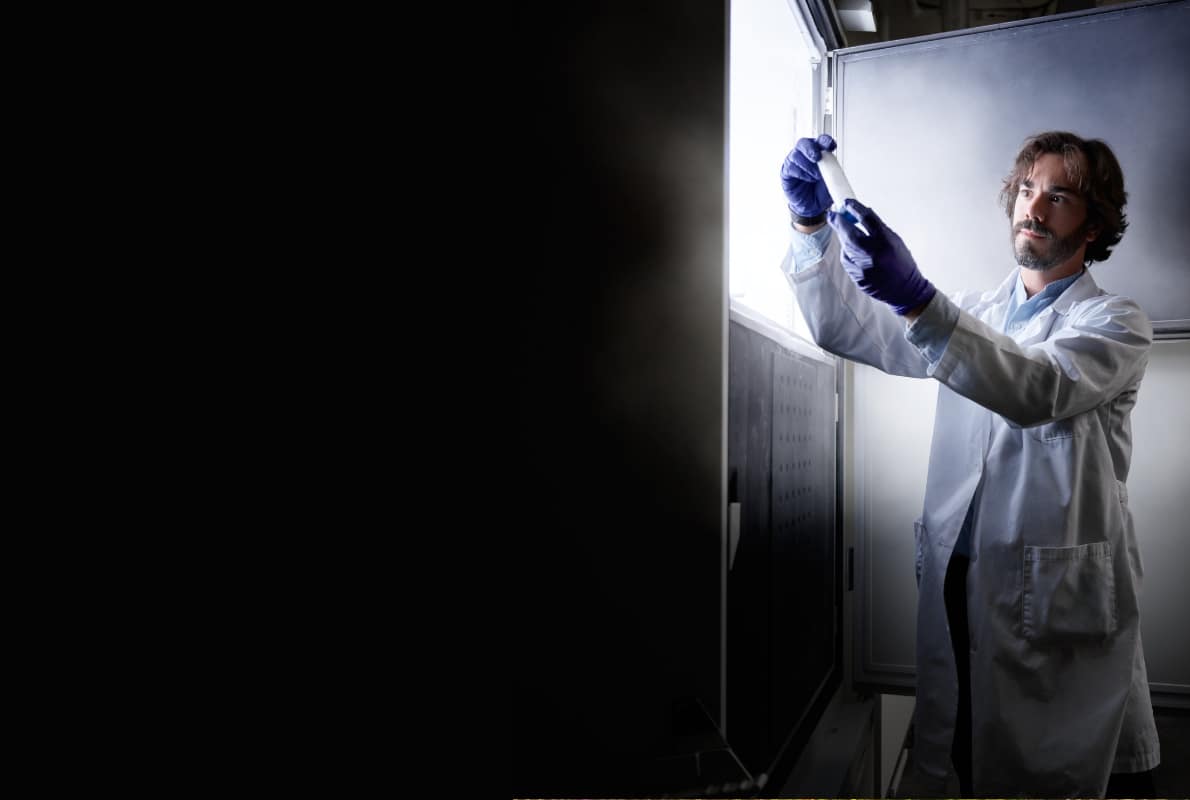 A researcher in a lab coat holds a sample next to a freezer