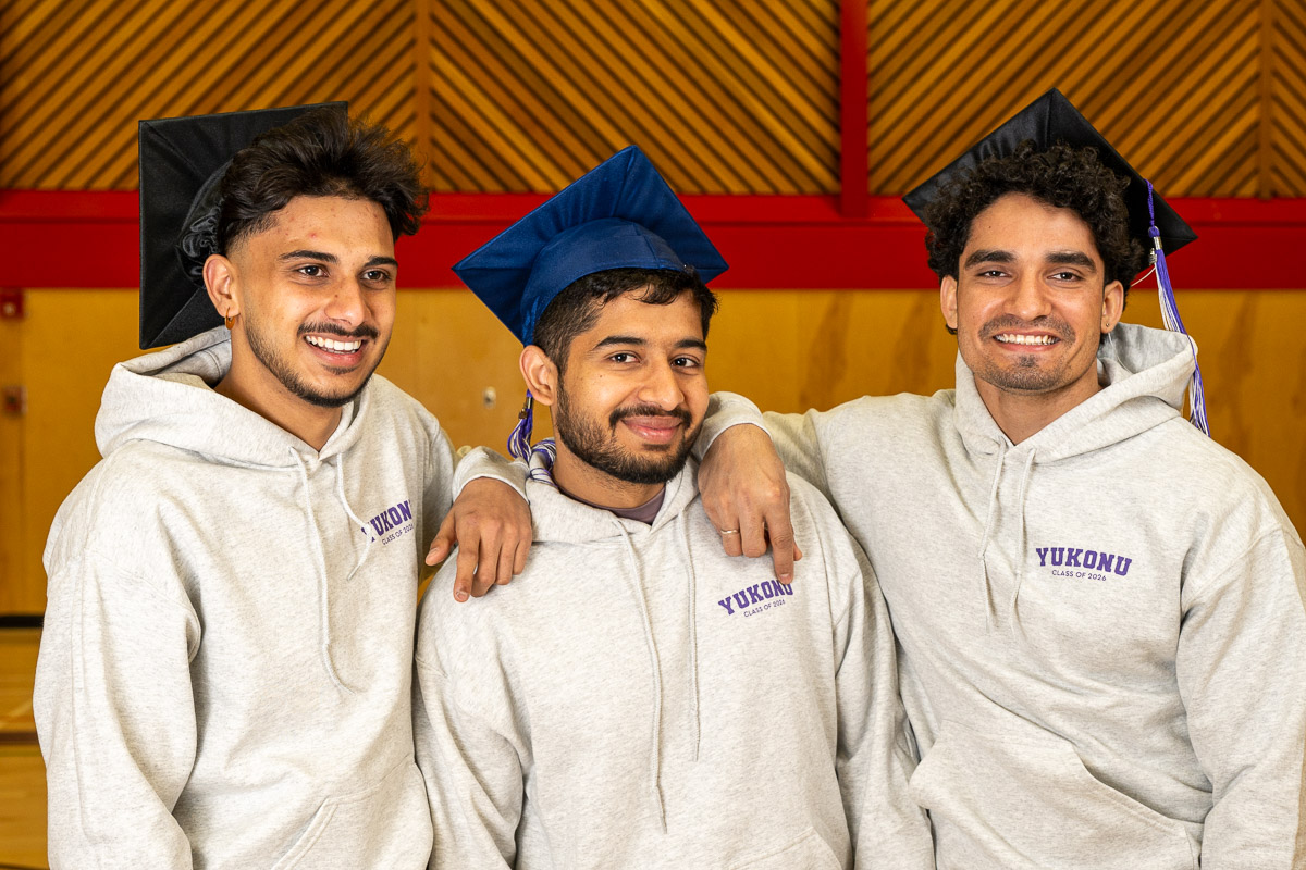 Three men wearing mortarboards and grey hoodies with YukonU Class of 2026 printed on them