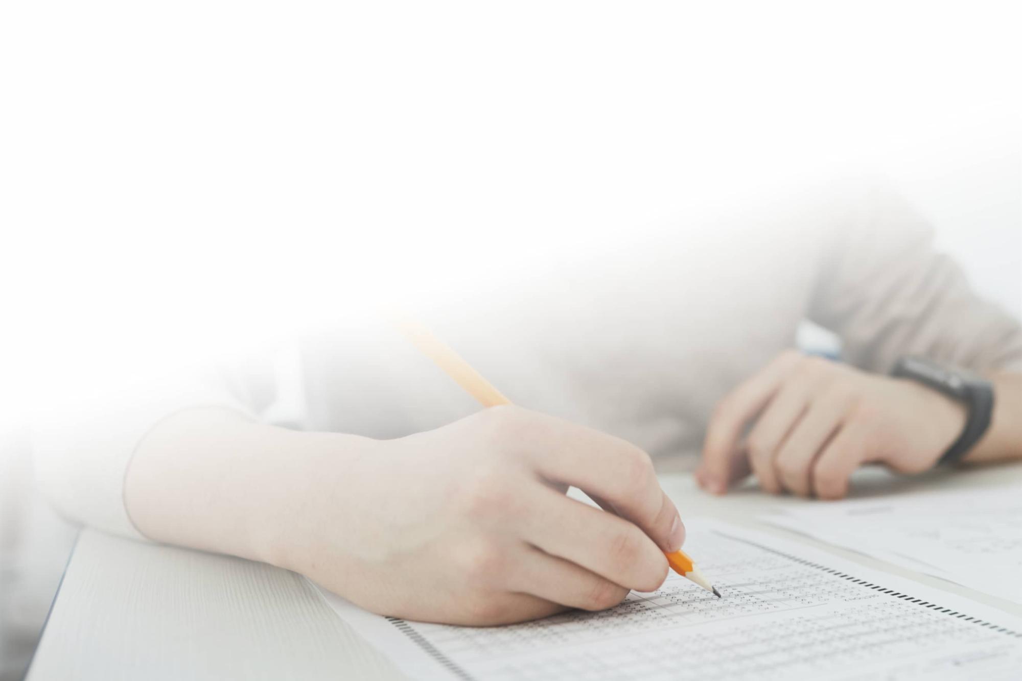 Man&apos;s hand writing a multiple choice exam with a pencil