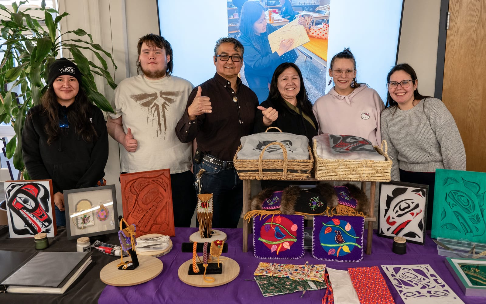 Students and instructors smiling and posing behind a table featuring a variety of handmade Yukon First Nations art pieces