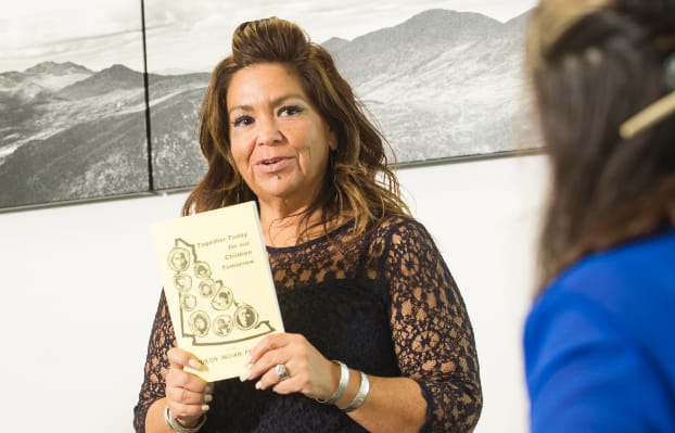 A woman standing in front of a meeting table holding up a copy of Together Today For Our Children Tomorrow