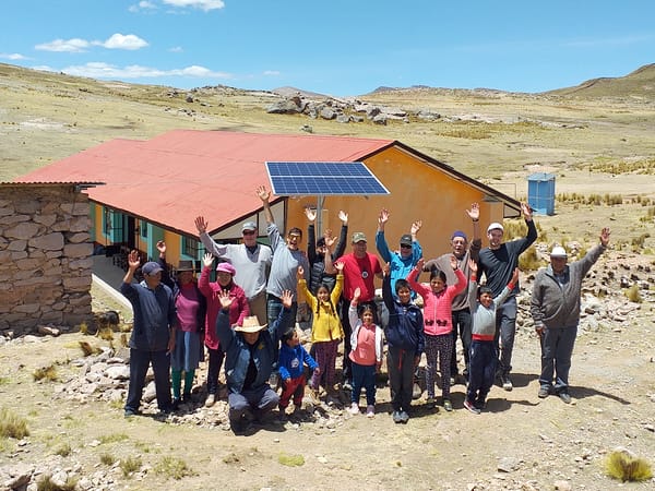 A group of people standing in front of a newly installed solar panel with their arms raised in the air