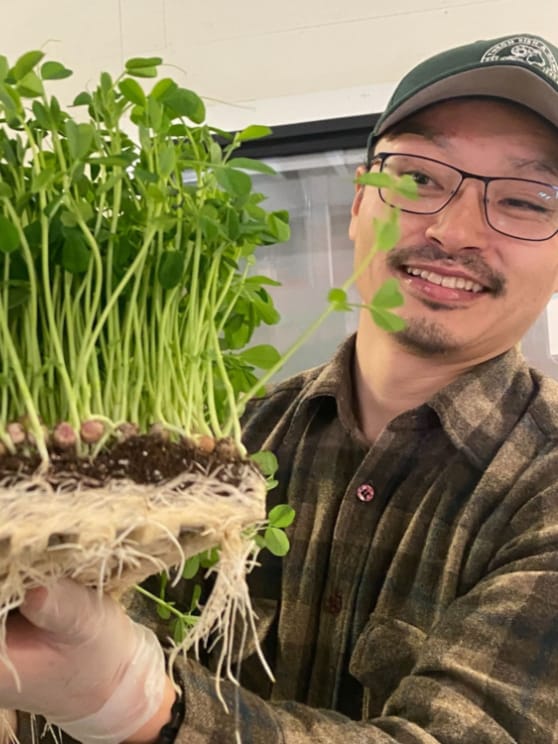 A man wearing glasses and a baseball cap holding up edible greens