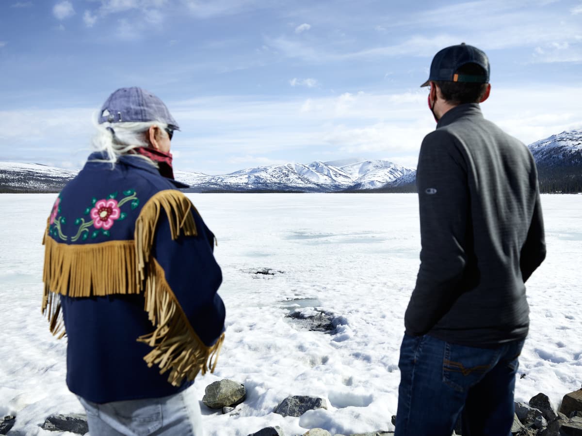 Two men looking out over a frozen lake with snow-covered mountains in the background