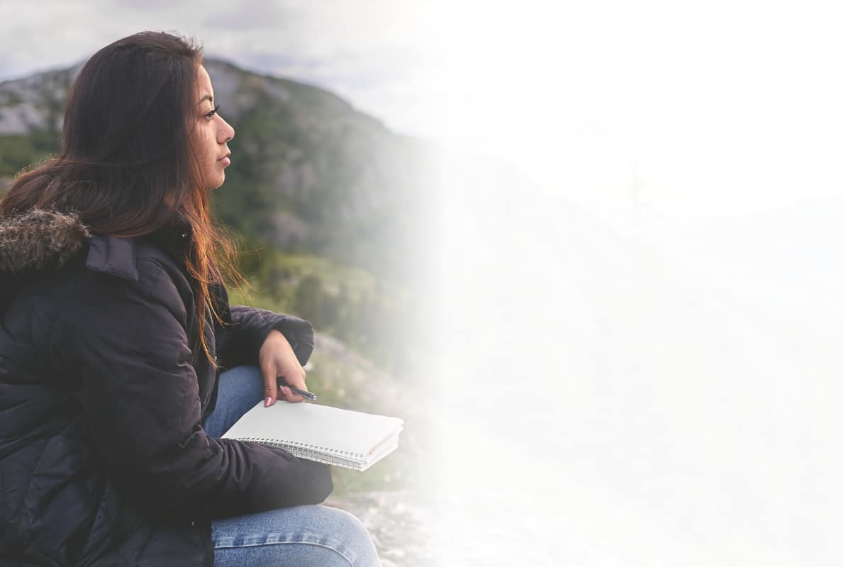 A student sitting outdoors with a notebook