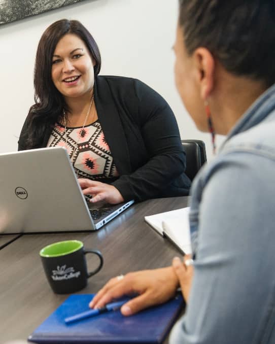 A woman with a laptop computer in conversation with another person
