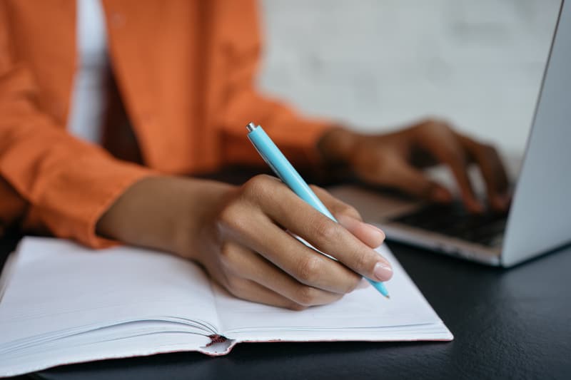 A hand holding a blue pen overing over the page in an open notebook