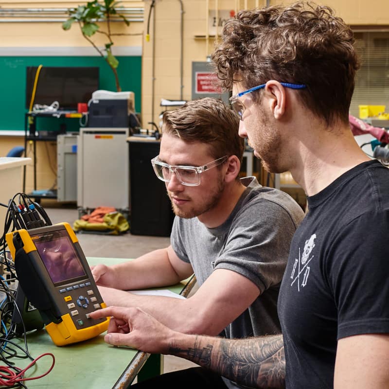 Two students in a trades class using electrical equipment