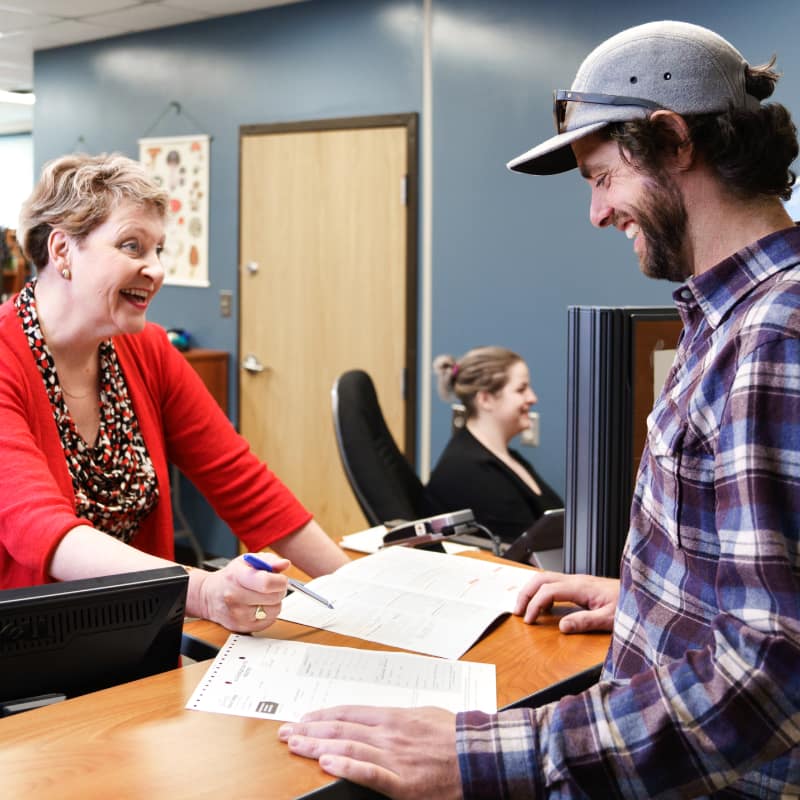 A student wearing a cap is helped with paperwork by a smiling woman