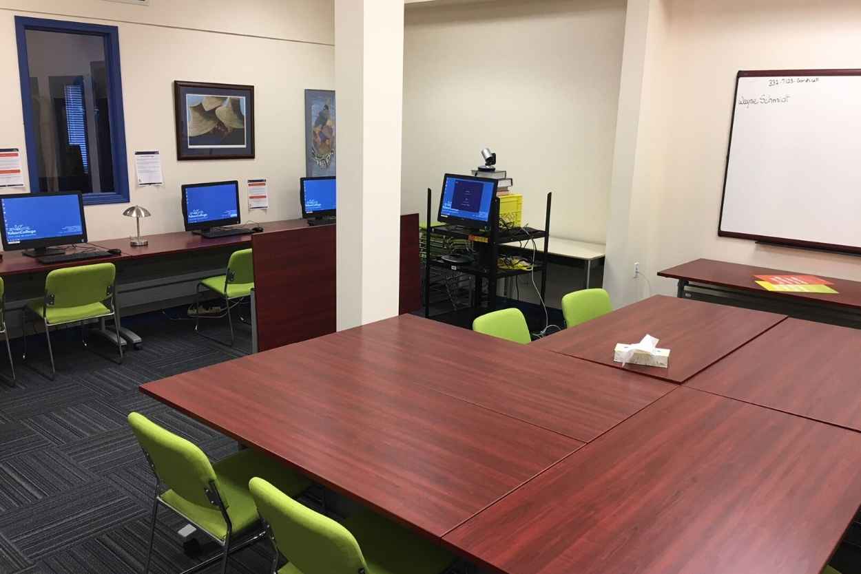 A computer lab with red meeting tables and green chairs with a whiteboard along the far wall
