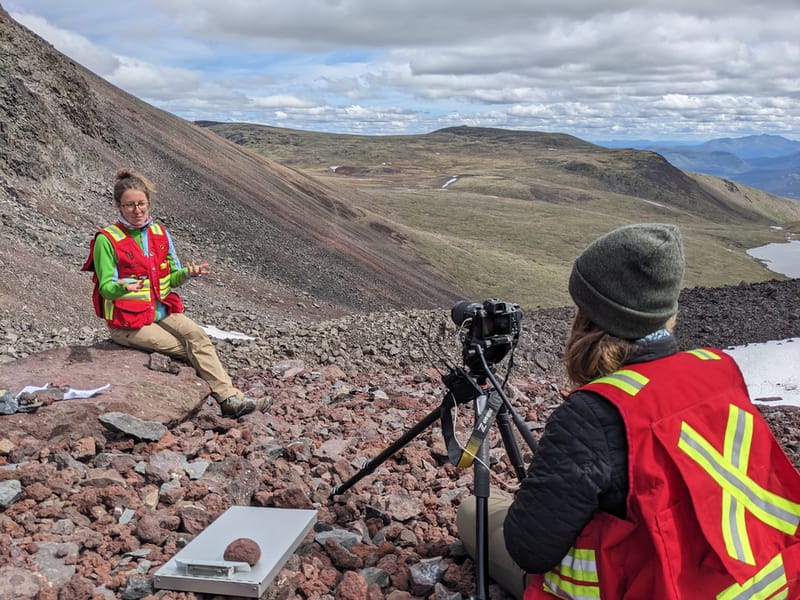 Two instructors in red vests recording a video on a rocky mountain slope