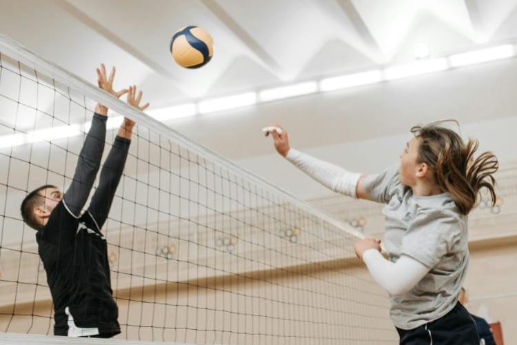 A man in a black shirt attempts to block a volleyball spiked by a woman in a grey shirt