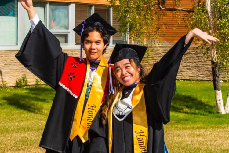 Two students wearing honours grad regalia celebrating outdoors