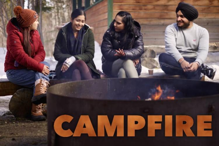 Four students sitting next to a campfire in a large fire pit