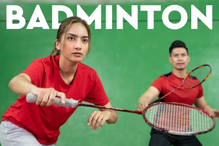 A woman and man in red shirts with badminton rackets in front of a green wall