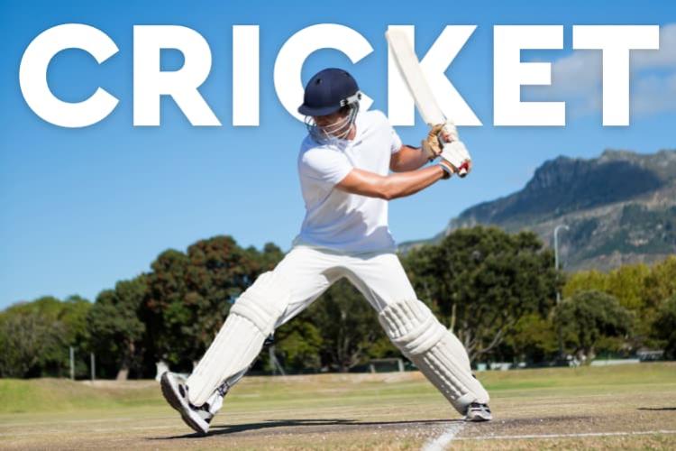 A man dressed in white with a blue helmet steps forward into a swing of a cricket bat.
