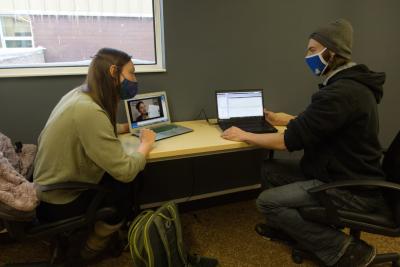 Two researchers wearing masks sharing a desk and working on laptops