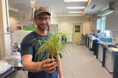 Ben stands in lab holding a plant