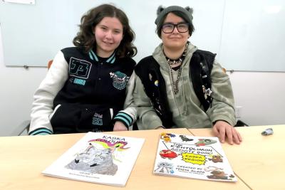 Two teenagers sitting at a desk with books they created