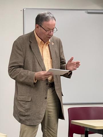 US Ambassador David L. Cohen stands at the front of a class and addresses students reading from a paper