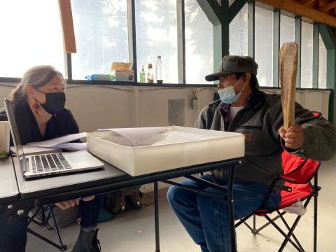 Man sitting holding a moose scapula next to a woman with a facemask on.