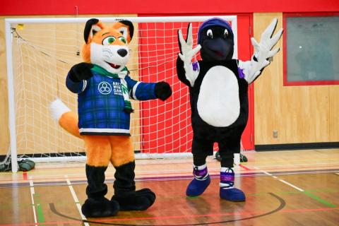 Arctic Winter Games 2026 mascot a fox named Michael Jay, and Yukon University mascot, a loon named Luna, celebrate together in the Yukon University gymnasium