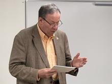 US Ambassador David L. Cohen stands at the front of a class and addresses students reading from a paper