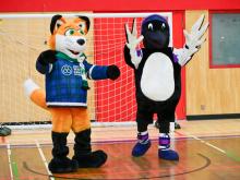 Arctic Winter Games 2026 mascot a fox named Michael Jay, and Yukon University mascot, a loon named Luna, celebrate together in the Yukon University gymnasium